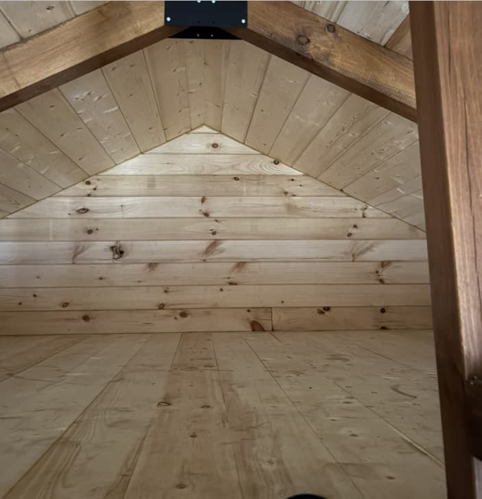 Cabin loft space with pitched pine ceiling, exposed dark wood beams, and natural wood flooring