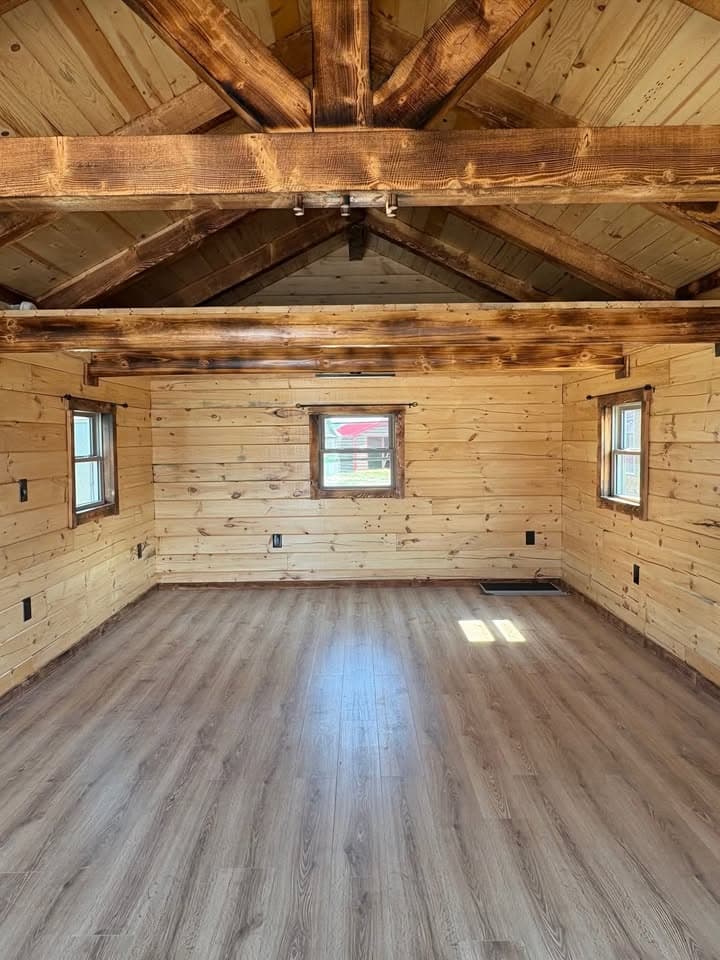 Rustic cabin interior with light wood paneling, exposed beam trusses, and wood laminate flooring