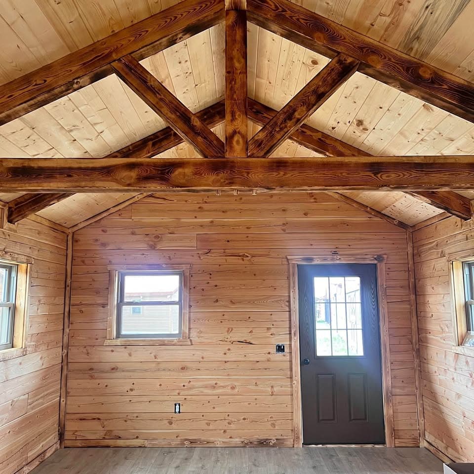 Rustic log cabin interior with natural knotty pine walls, vaulted ceiling, and dark-stained wooden trusses