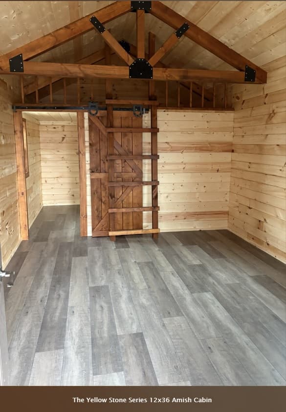 Yellowstone 12x36 cabin interior with rustic sliding barn door and loft with exposed timber trusses